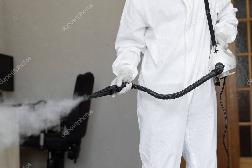 Disinfector in a protective suit conducts disinfection in home. professional disinfection against COVID-19, coronavirus. in clothing protecting from chemical poisoning in the industry