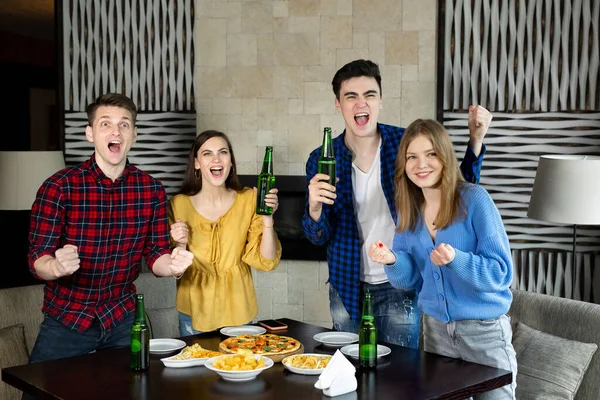 Feliz animado alegre quatro amigos assistindo futebol na TV em um pub beber bebidas alcoólicas comer pizza. — Fotografia de Stock