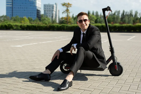 Νέος, όμορφος επιχειρηματίας με κοστούμι κάθεται σε ένα ηλεκτρικό σκούτερ και γελάει — Φωτογραφία Αρχείου