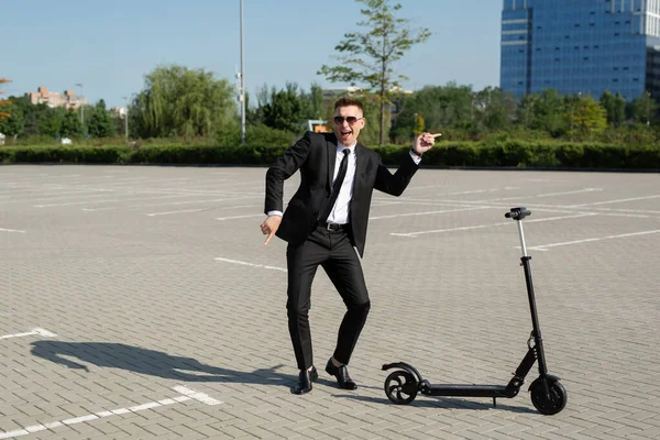 Joven hombre de negocios guapo en un traje monta un scooter eléctrico alrededor de la ciudad y se ríe — Foto de Stock