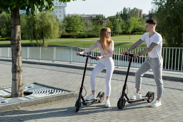 Meisje en jongen lopen op elektrische scooters door de stad, een paar verliefd op scooters — Stockfoto