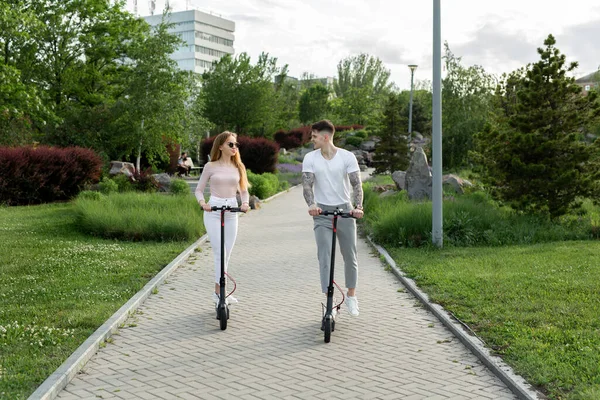 Jovem casal de férias se divertindo dirigindo scooter elétrico através do parque. — Fotografia de Stock