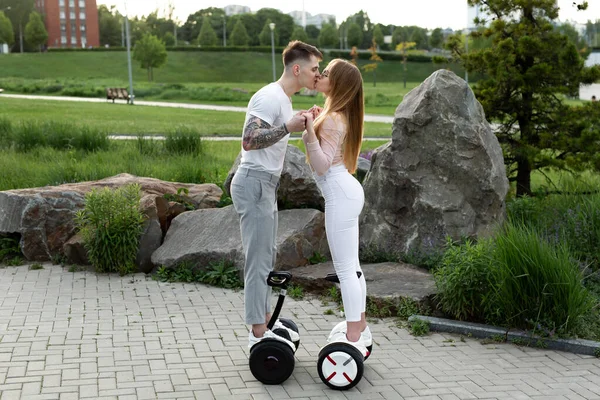 Joven y una mujer montan en un hoverboard y se besan en el parque. —  Fotos de Stock