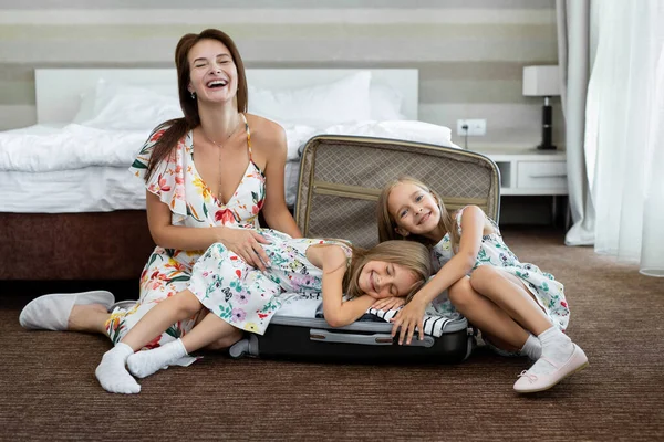Joven madre y sus hijas gemelas con una maleta en una habitación de hotel — Foto de Stock