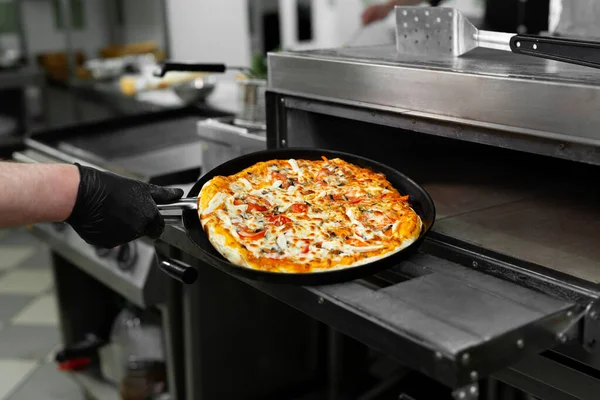 Pizza chef puts pizza in the oven to bake in the oven in the restaurant kitchen. Stock Picture