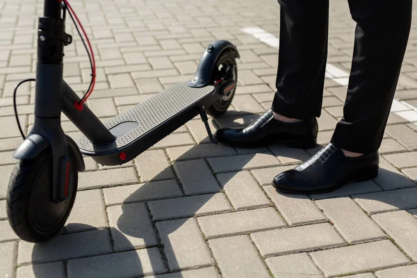 Primer plano de los pies de un hombre en un traje de negocios y zapatos cerca de una scooter eléctrico —  Fotos de Stock