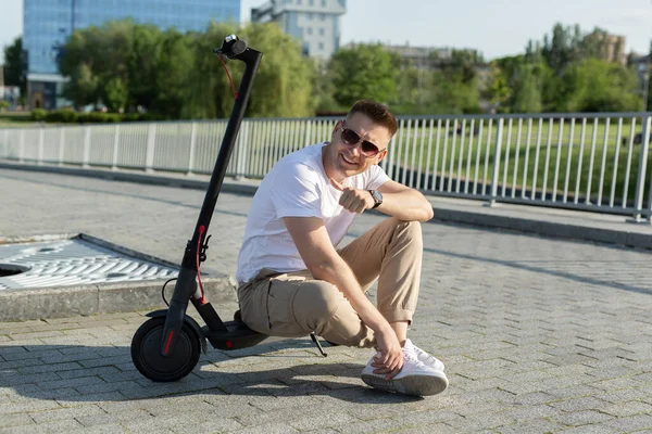 Alegre hombre está sentado en un scooter eléctrico en un parque. — Foto de Stock