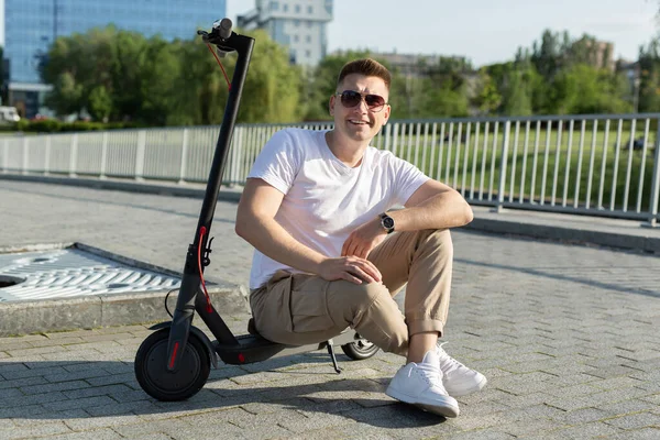 L'uomo allegro è seduto su uno scooter elettrico in un parco. — Foto Stock