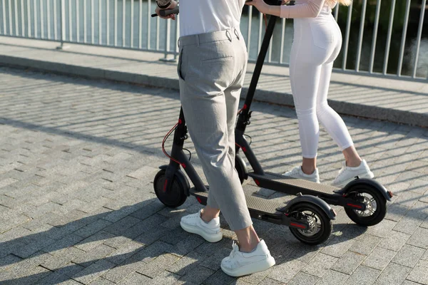 Um par de homens e mulheres estão andando no parque e empurrando scooters elétricos — Fotografia de Stock