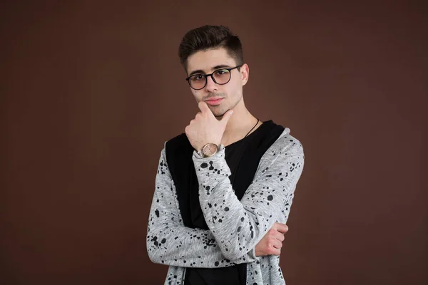 Młody człowiek w depresji. Stylowy student nosi okrągłe okulary, ma modną fryzurę, wygląda pewnie, odizolowany na brązowym tle. Ludzie i wyrażenia ludzkie. — Zdjęcie stockowe