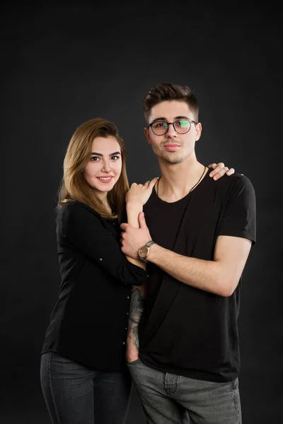 Retrato de jovem casal em roupas pretas vestindo óculos da moda e posando sobre fundo preto — Fotografia de Stock