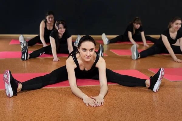 Mladé atletické dívky se zahřívají před tréninkem v tělocvičně. Flexibilita dívky dělat cvičení na podlaze moderní tělocvičny. — Stock fotografie