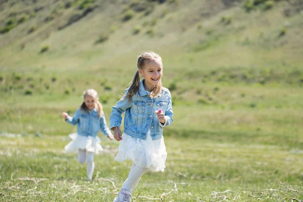 Dos hermanitas gemelas corren y giran en el prado —  Fotos de Stock