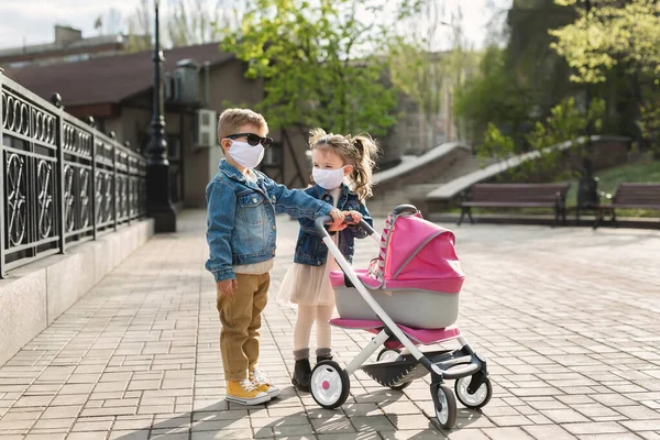 Junge und Mädchen gehen mit Kinderwagen und Mundschutz. Konzept der Familie. Coronavirus, covid-19. — Stockfoto