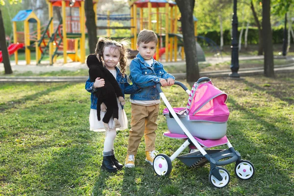 Kleine jongen en klein meisje baby lopen met een wandelwagen voor poppen — Stockfoto