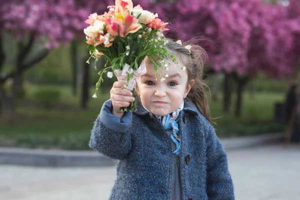 Niña en un parque en primavera amenaza a la cámara y agita un ramo de flores —  Fotos de Stock
