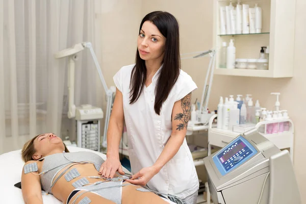 Profesjonalny kosmetyk sprawia, że masaż antycellulitowy do młodej kobiety z pomocą aparatu biostymulującego. Kobieta w piękno medyczne spa centrum antycellulitowe elektrostymulacji terapii. — Zdjęcie stockowe