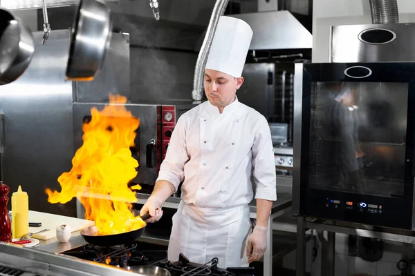 Séf főzés lánggal egy serpenyőben a konyhában tűzhely. — Stock Fotó
