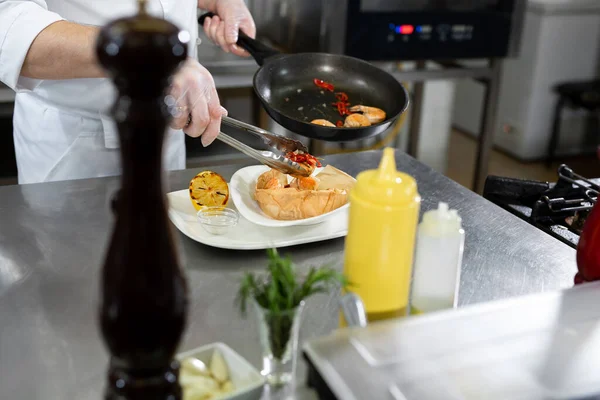 Hermoso hombre chef preparando plato con camarones en la mesa en la cocina. — Foto de Stock