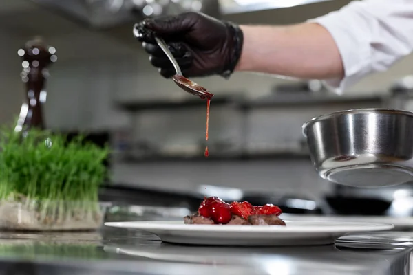 La mano sostiene la cuchara sobre la carne. Salsa de color rojo. Deliciosos medallones con fresas. — Foto de Stock