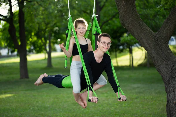 Man and a little girl do group yoga in a hammock in the park. — Stock Photo, Image