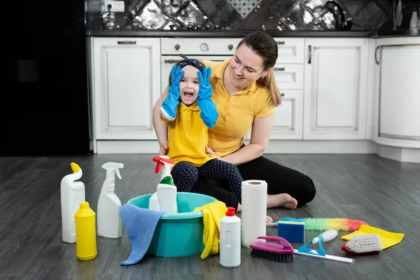 Szczęśliwa matka i jej córka zakładają gumowe rękawiczki i cieszą się sprzątaniem, dobrze się razem bawią. — Zdjęcie stockowe