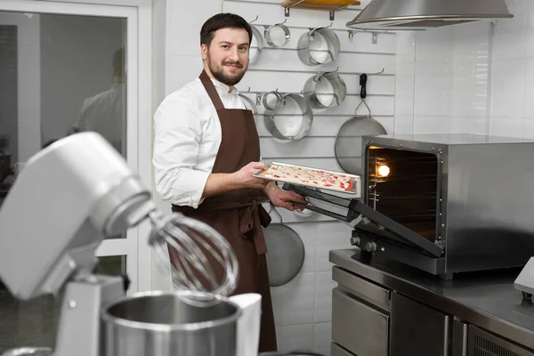 Uomo pasticcere mette la pasta di spugna in forno. — Foto Stock
