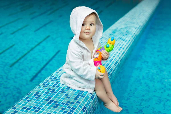 Ein Kleinkind, ein kleines Kind in einem Badetuch im Pool mit einem hellen Spielzeug in den Händen — Stockfoto