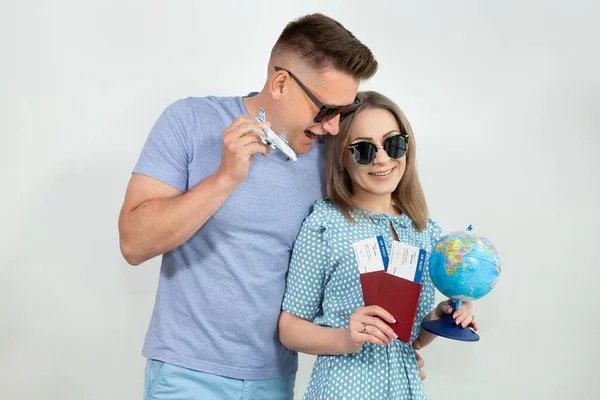 Emocionados jóvenes turistas en gafas de sol, un chico y una chica aislados en un fondo blanco con un globo, pasaportes, boletos y un avión modelo en sus manos — Foto de Stock
