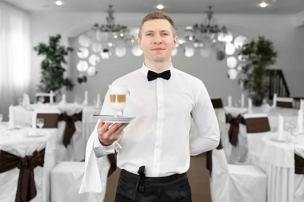 Portré egy mosolygó pincérről egy étteremben, tejeskávét szolgál fel egy vendégnek. — Stock Fotó