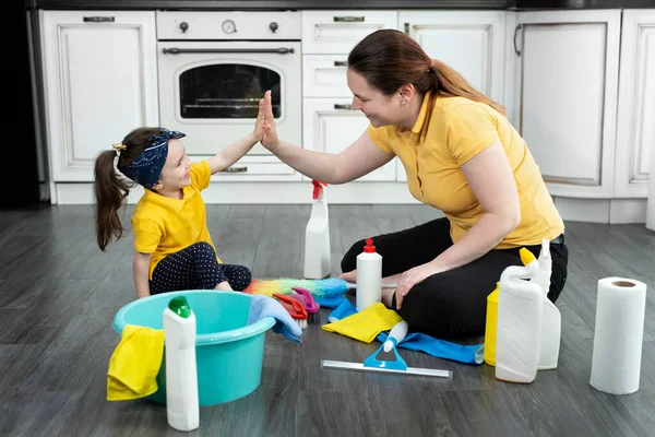 Güzel genç bir kadın ve küçük kızı yerde oturup evlerini temizlerken eğleniyorlar.. — Stok fotoğraf