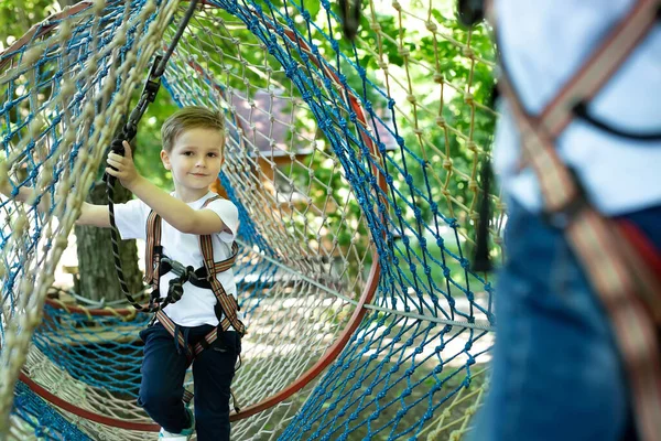 Portrait of a little boy in climbing gear in a rope park, holding a rope with a carbine — Stock Photo, Image