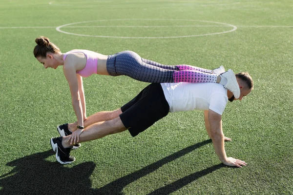 Joven y una chica entrenar al aire libre en el verano, un hombre hace push-UPS y una chica se para en su espalda y hombros. Estilo de vida deportivo. — Foto de Stock