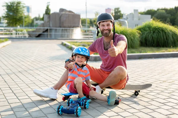 Kasklı mutlu baba ve oğul, kaykayların üzerinde otururken eldivenle kontrol edilen robot bir arabayla parkta oynuyorlar.