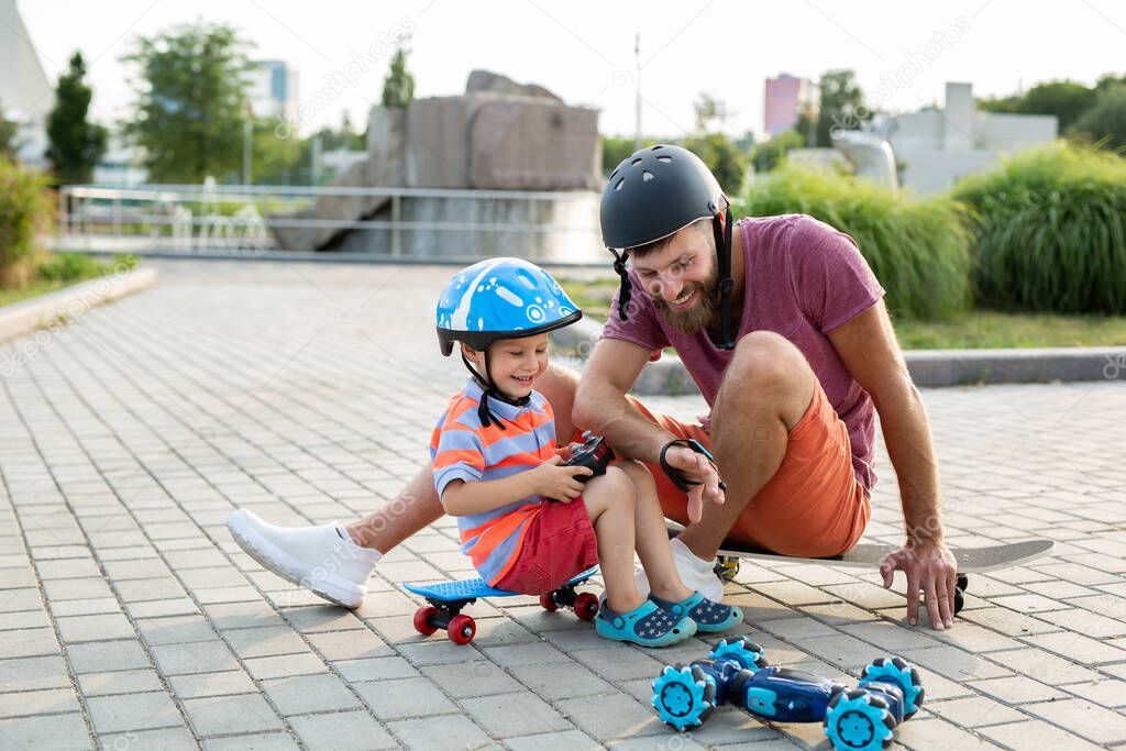 Happy father and son in helmets play in the Park with a robot car that is controlled by a glove while sitting on skateboards