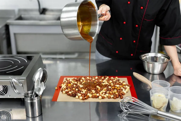 Pastelero vierte jarabe caliente, caramelo sobre avellanas para hacer praliné. — Foto de Stock
