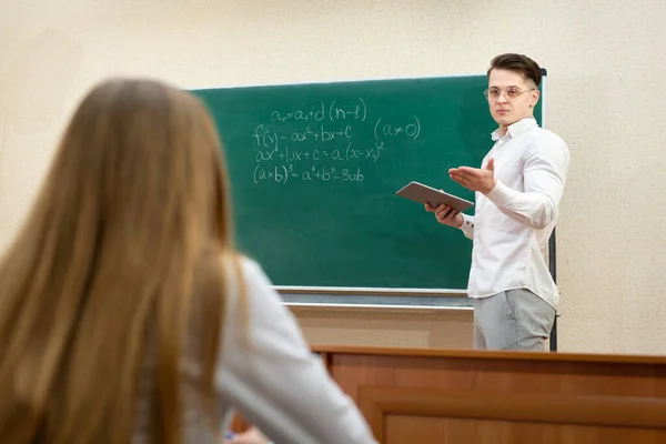 Ung student med glasögon och en surfplatta svarpå svarta tavlan — Stockfoto