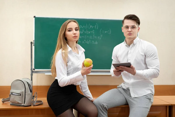 Atrakcyjni młodzi studenci siedzą na biurku w klasie podczas przerwy — Zdjęcie stockowe