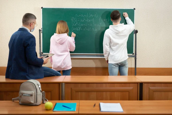 Insegnanti e studenti indossano maschere protettive vicino alla lavagna durante la quarantena. Covid-19 — Foto Stock