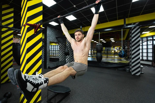 Hombre joven flexionando los músculos abdominales en la barra de pull-up en el gimnasio. — Foto de Stock