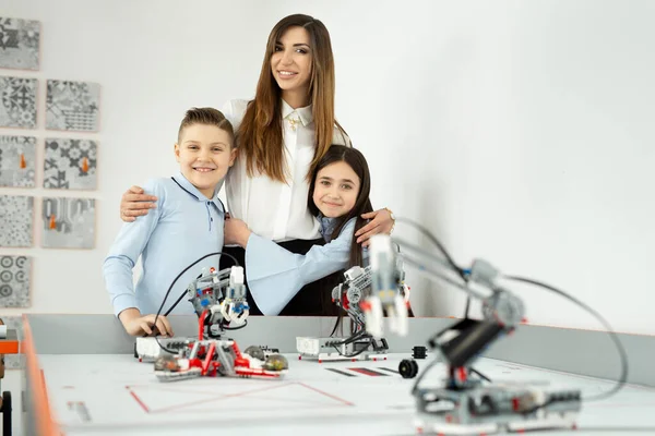 Jeune belle mère avec son fils et sa fille posent à l'école de robotique avec des robots du constructeur — Photo