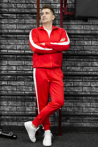 Λεπτός άντρας με κόκκινη φόρμα ποζάρει στον τοίχο του γυμναστηρίου. — Φωτογραφία Αρχείου