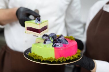 Bir parça kremalı kekin yakın çekimi erkek bir pasta şefinin ellerinde.