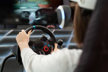 Direksiyonu elinde tutan ve konsolda bilgisayar oyunu oynayan sanal gerçeklik gözlüklü genç bir kızın ellerine yakın çekim.