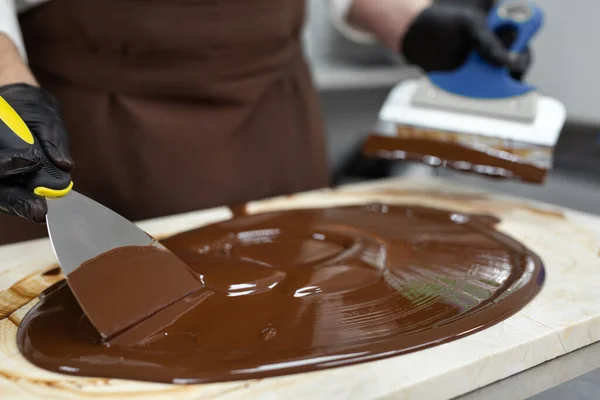 Мужской шоколад использует лопатку, чтобы перемешать закаленный жидкий шоколад на гранитном столе.. — стоковое фото