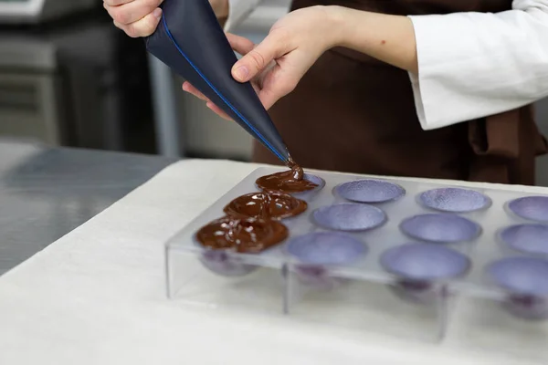 Primer plano de las manos chocolateros verter chocolate en los moldes. La bolsa de pastelería de los chefs vierte chocolate caliente derretido en un molde de silicona. — Foto de Stock