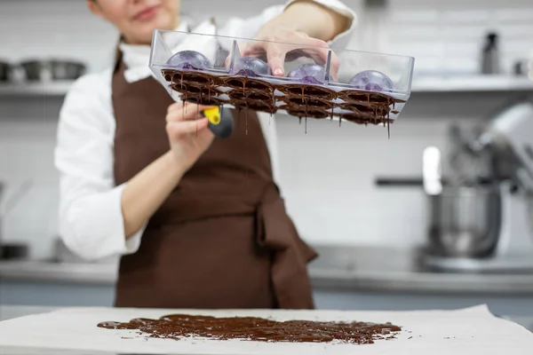 Chef o chocolatero hace chocolates dulces en una cocina profesional. Voltea el molde y vierte el resto del chocolate sobre la mesa. — Foto de Stock