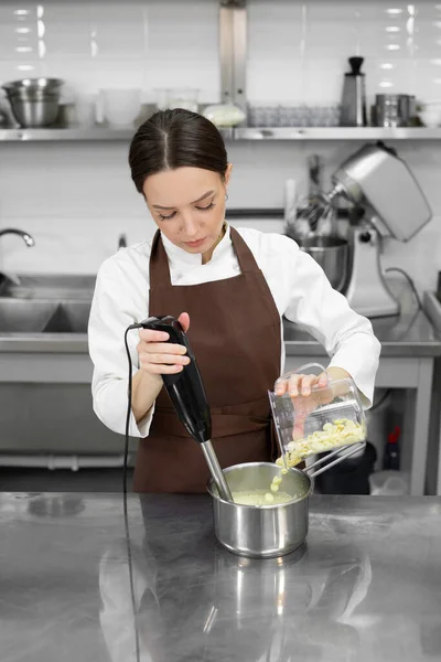 Female pastry chef whips up a mirror icing with white chocolate for a cake with a blender