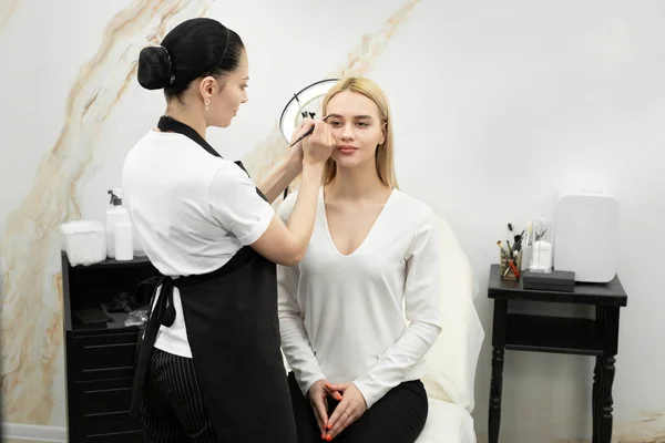 Artista de maquillaje cosmetólogo pinta los ojos de una joven mujer hermosa en el salón con un lápiz — Foto de Stock