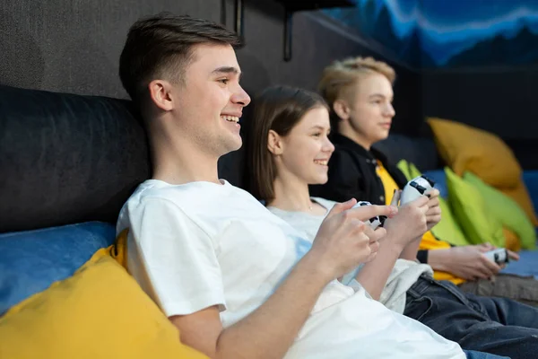 Группа друзей подростков, мальчиков и девочек, играющих в видеоигры на консоли в игровом клубе — стоковое фото